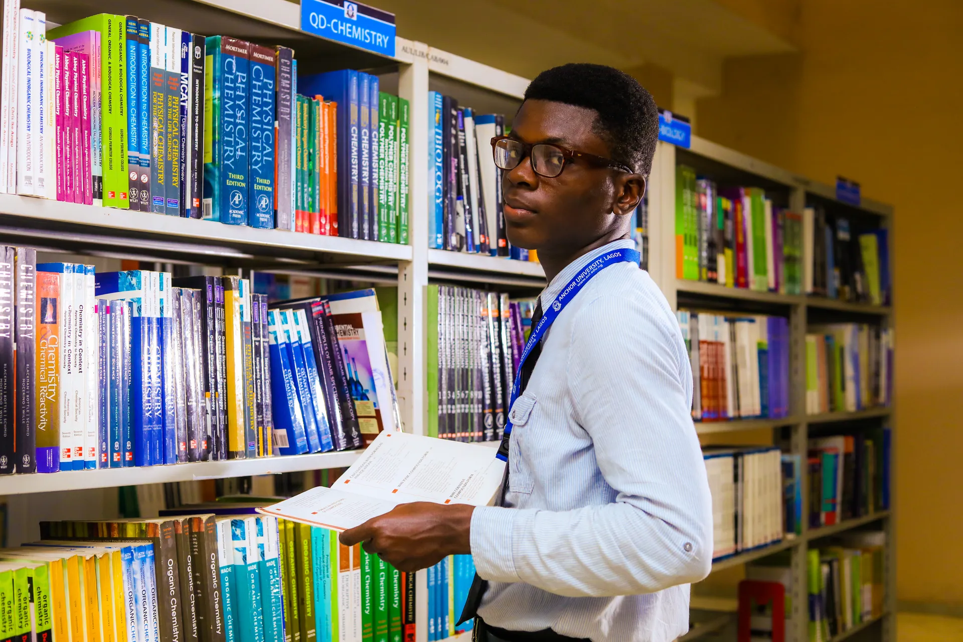 Student reading beside library bookshelves